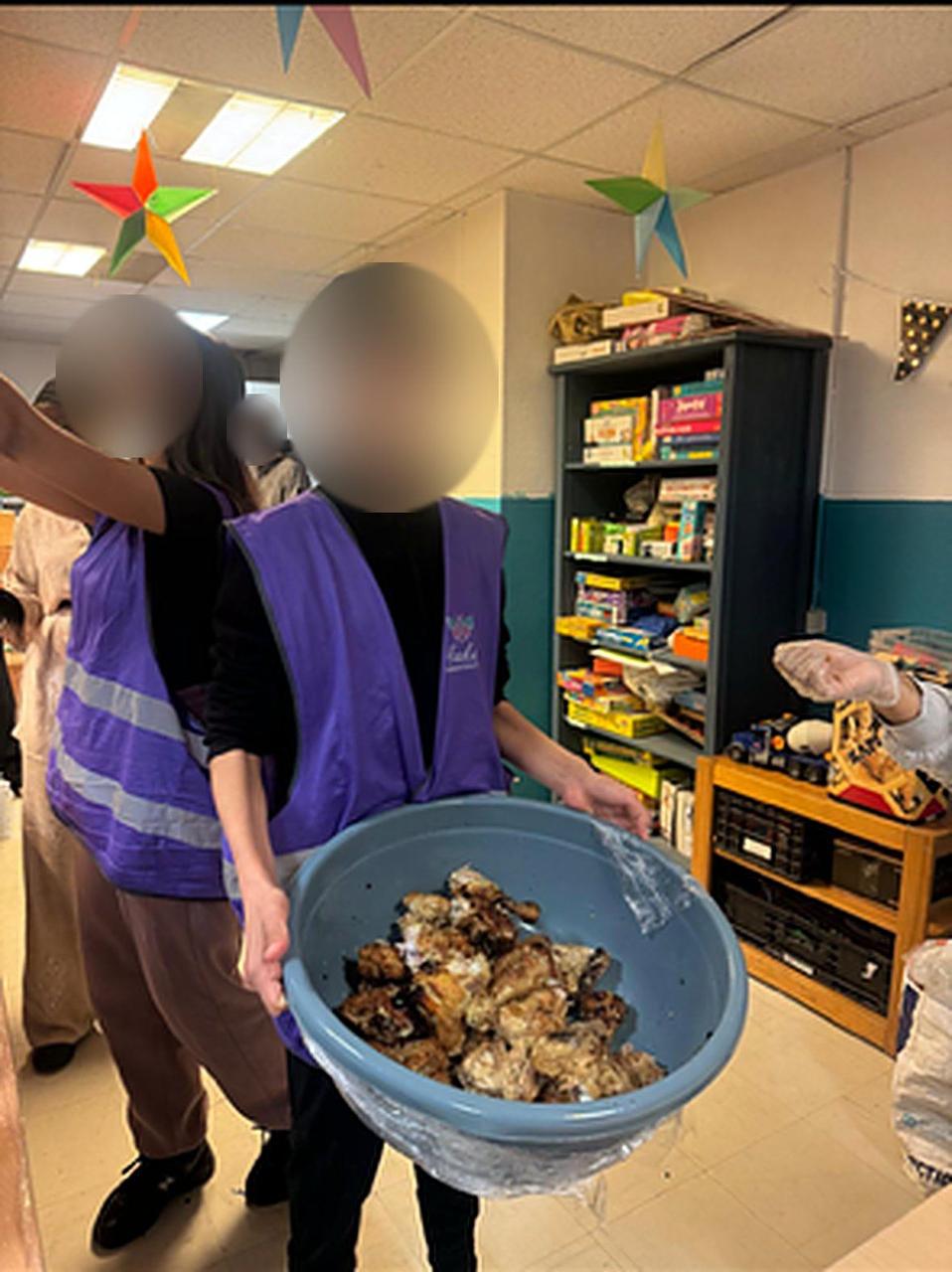 Des jeunes en chasuble violette préparent les repas solidaires, visages floutés.