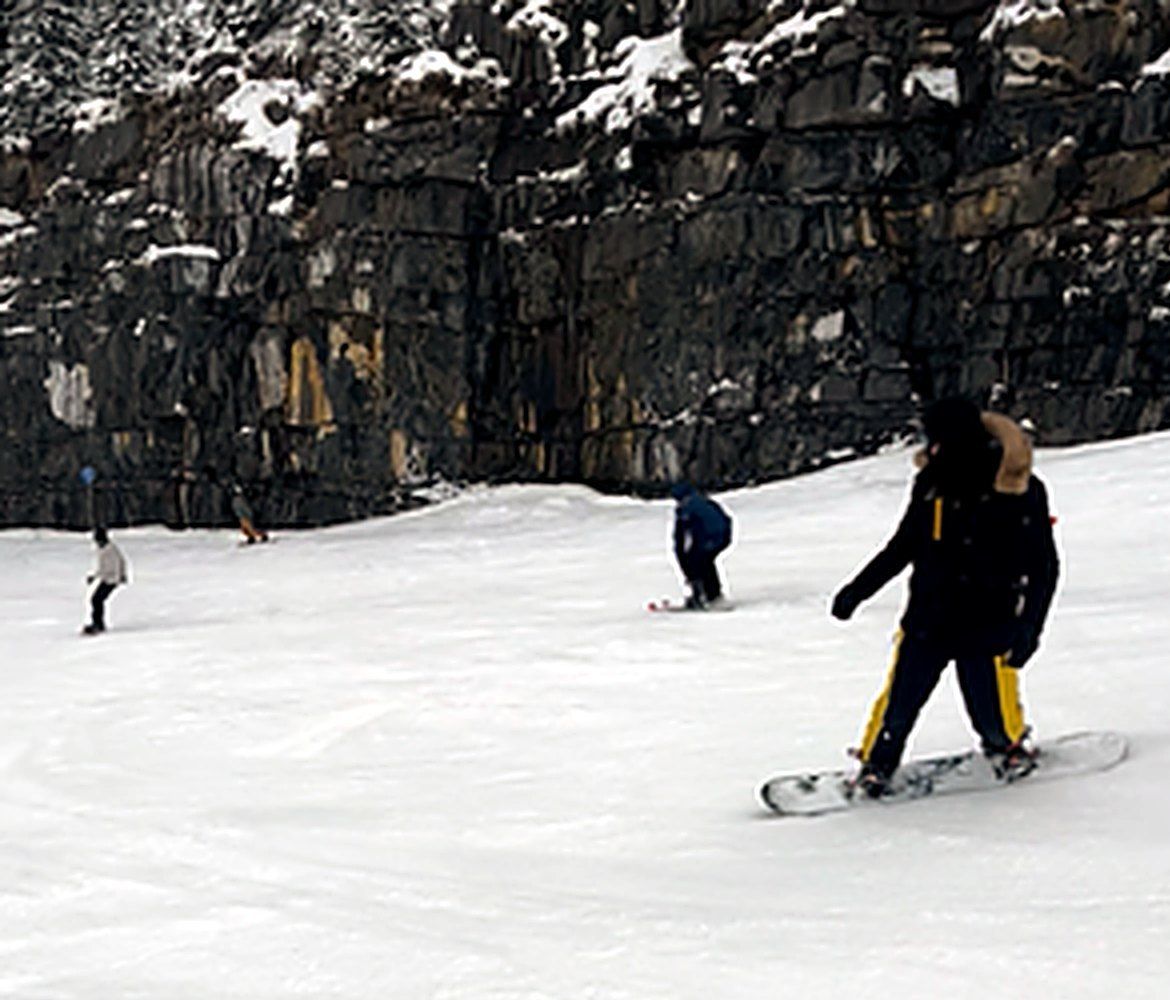 Un jeune descend une piste en snowboard au pied d'une falaise enneigée.