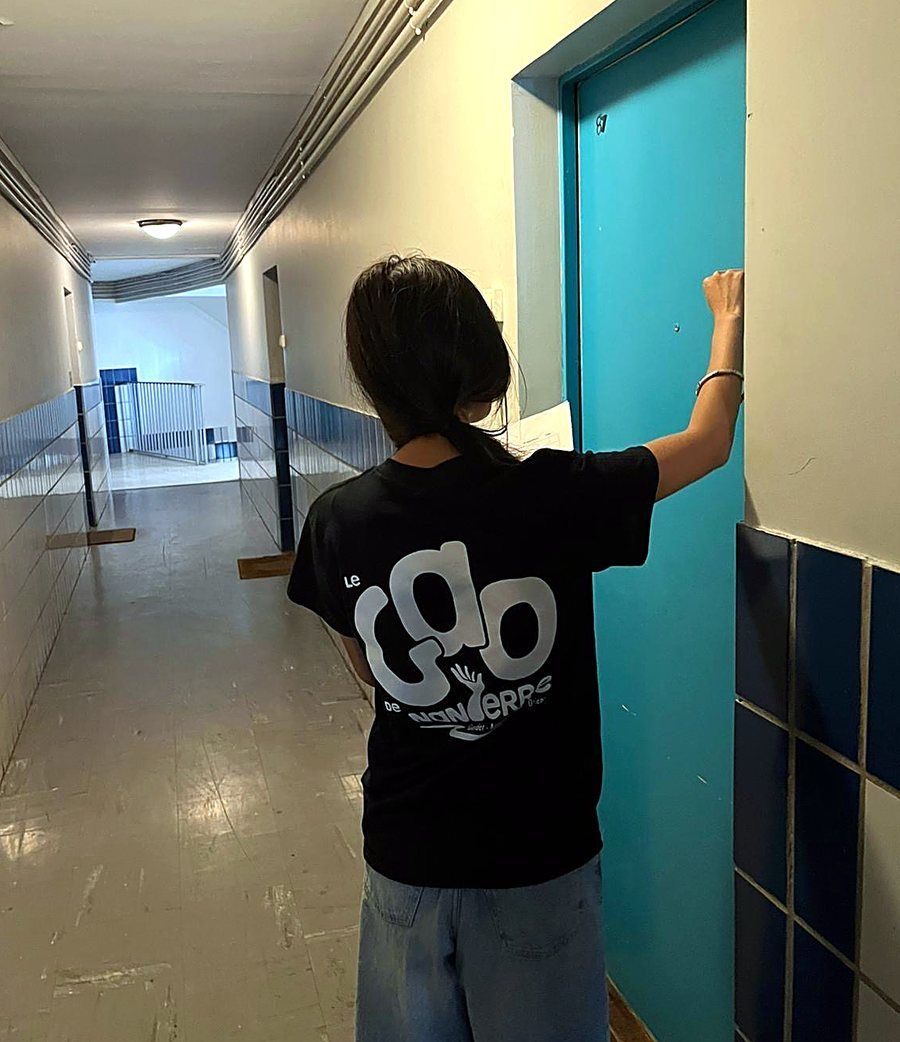 Une jeune avec le t-shirt du GAO frappe à la porte d'un appartement, de dos.